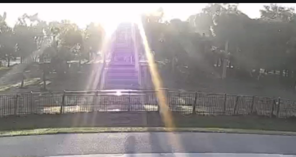 Golden and violet rays of sunlight forming ascending rectangular reflections over an empty fenced pasture.